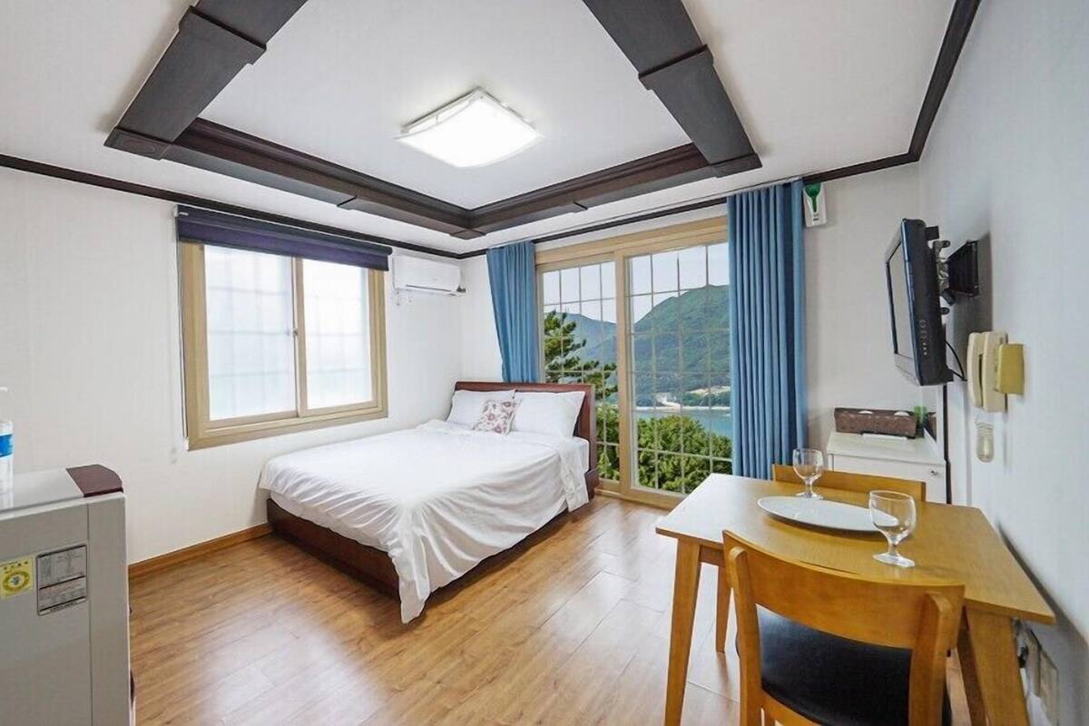 A hotel room with a bed, a desk with a chair, a window with a view, and a ceiling light.