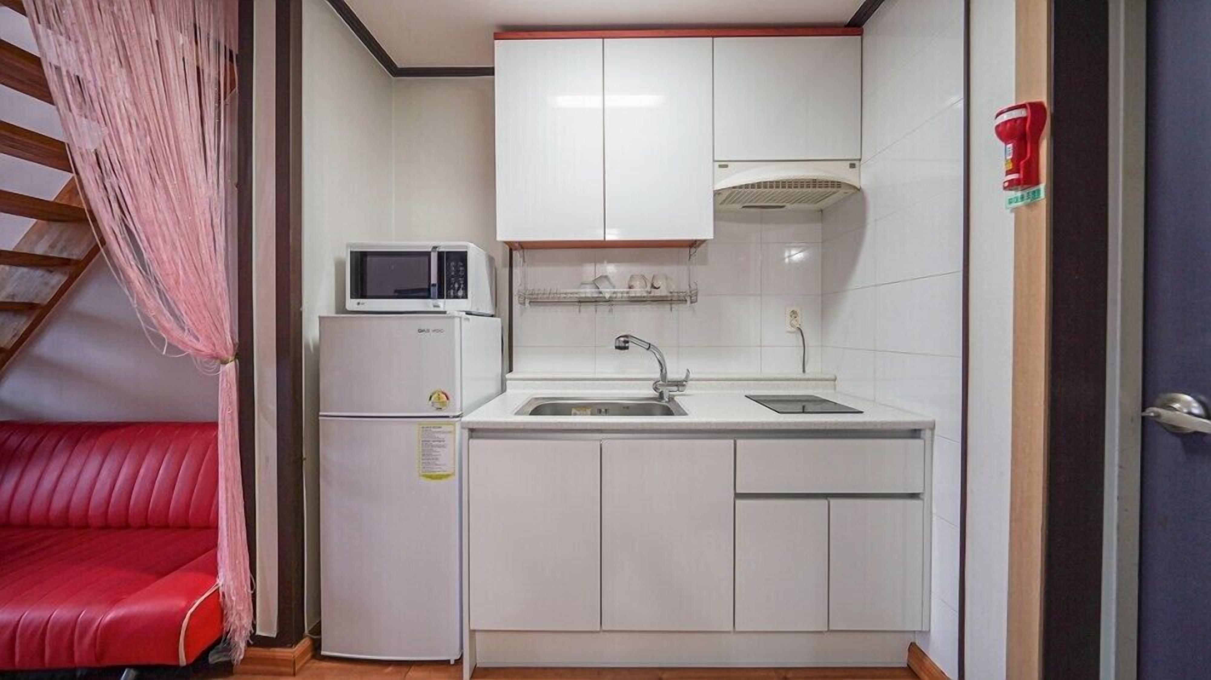 A compact kitchen with white cabinets, a microwave, a sink, and a small refrigerator.