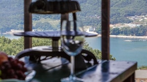 A table with a wine glass and grapes, overlooking a lake and forested area. - Geoje Cheongsol Pension (Geoje)