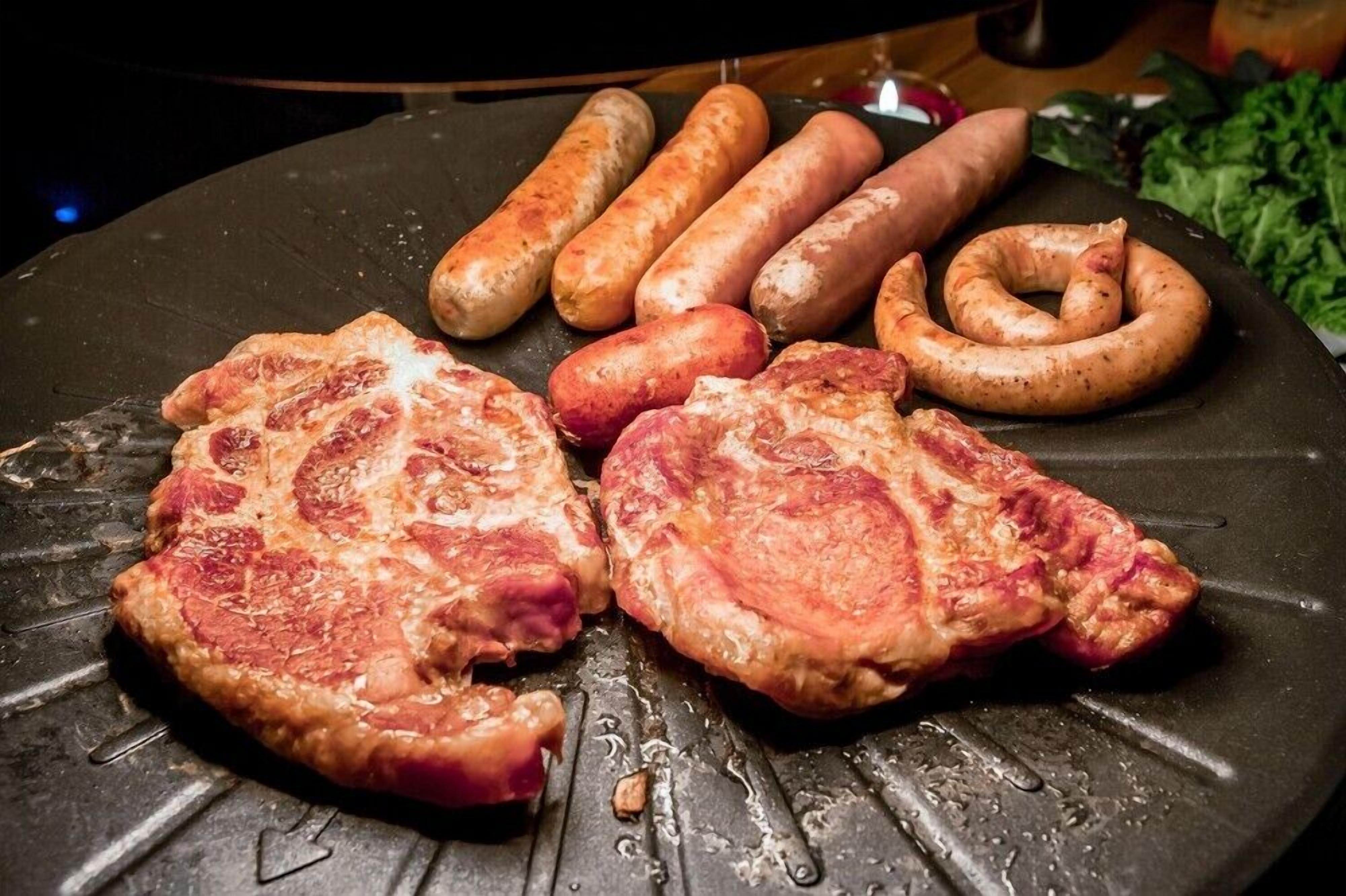 Una parrilla con dos filetes y varias salchichas.