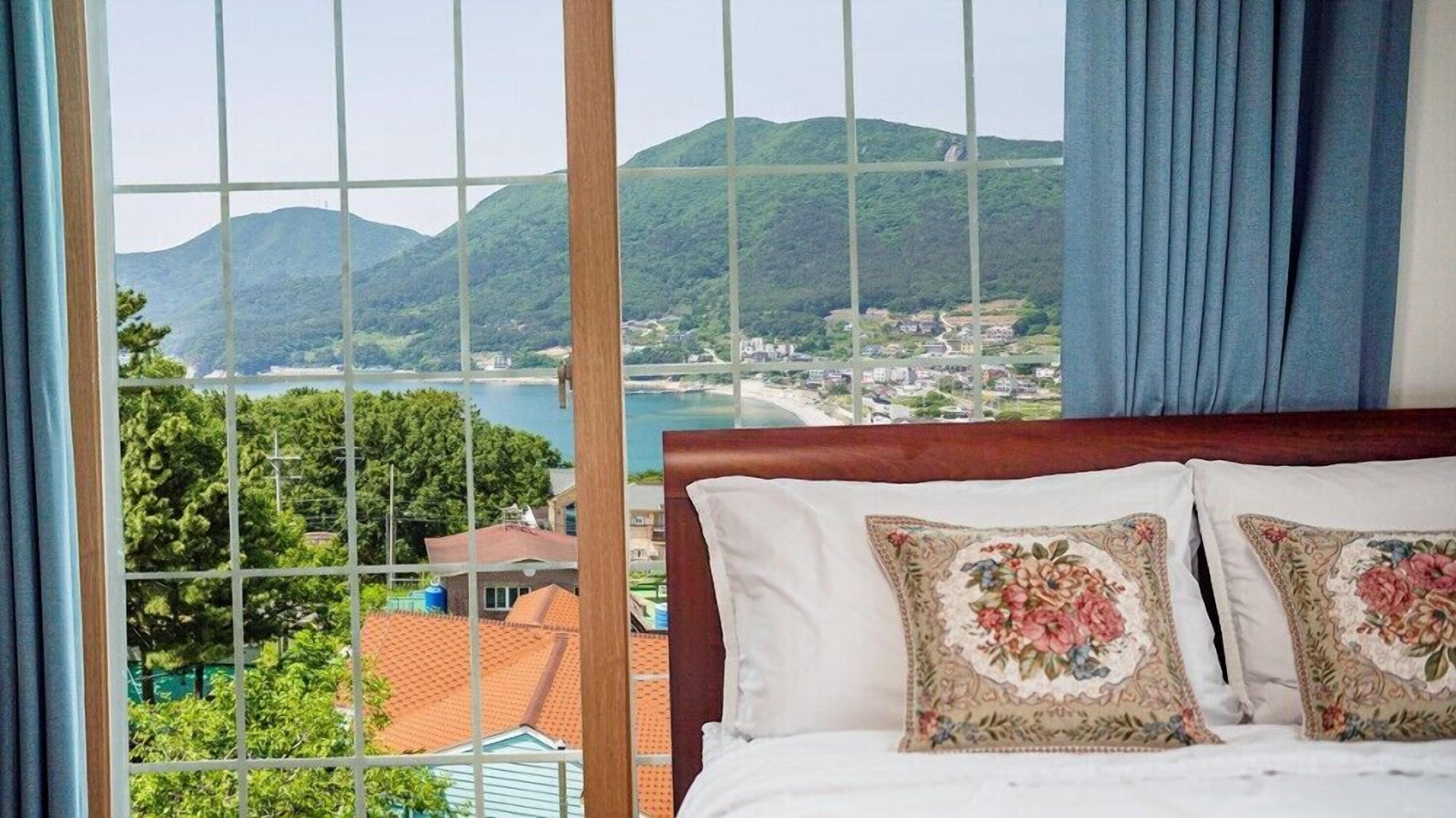 Camera da letto con una grande finestra che si affaccia su una località costiera e montagne.