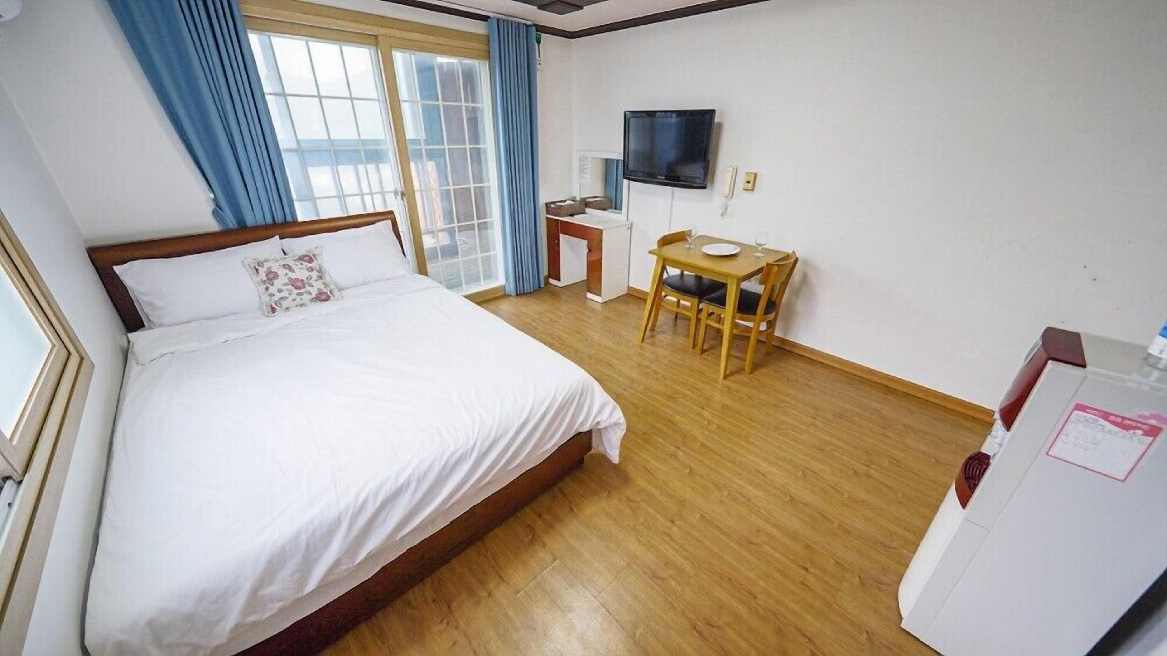 A hotel room with a large bed, a desk with a chair, a TV, and a window with curtains.