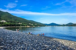 A pebbled beach with people relaxing by the water, surrounded by hills and a clear sky. - Geoje Cheongsol Pension (Geoje)