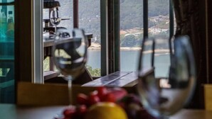 A table with a bowl of fruit and wine glasses, a bottle, and a view of a lake and hills through a window. - Geoje Cheongsol Pension (Geoje)