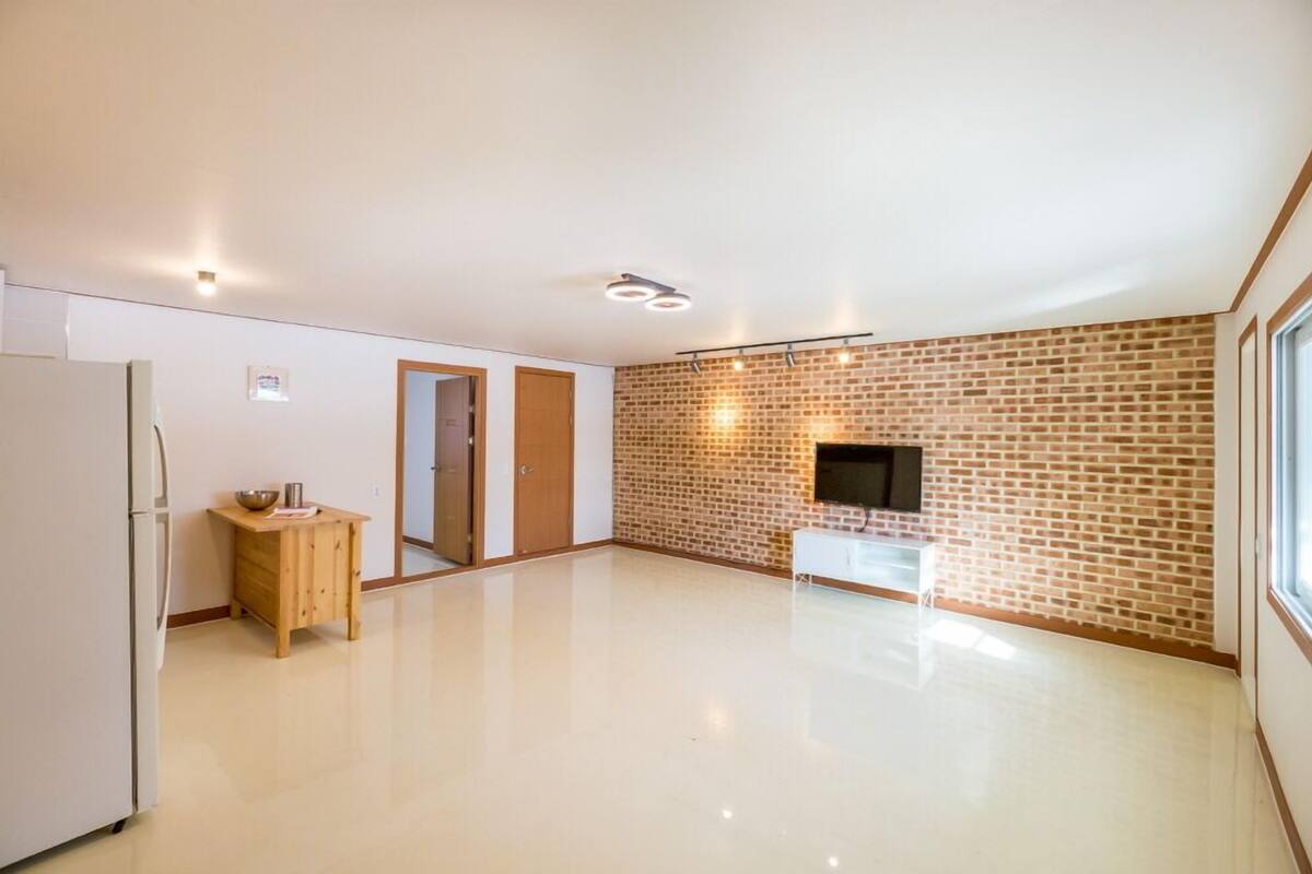 A spacious, modern kitchen with a brick accent wall, a refrigerator, a wooden cabinet, and a white countertop.