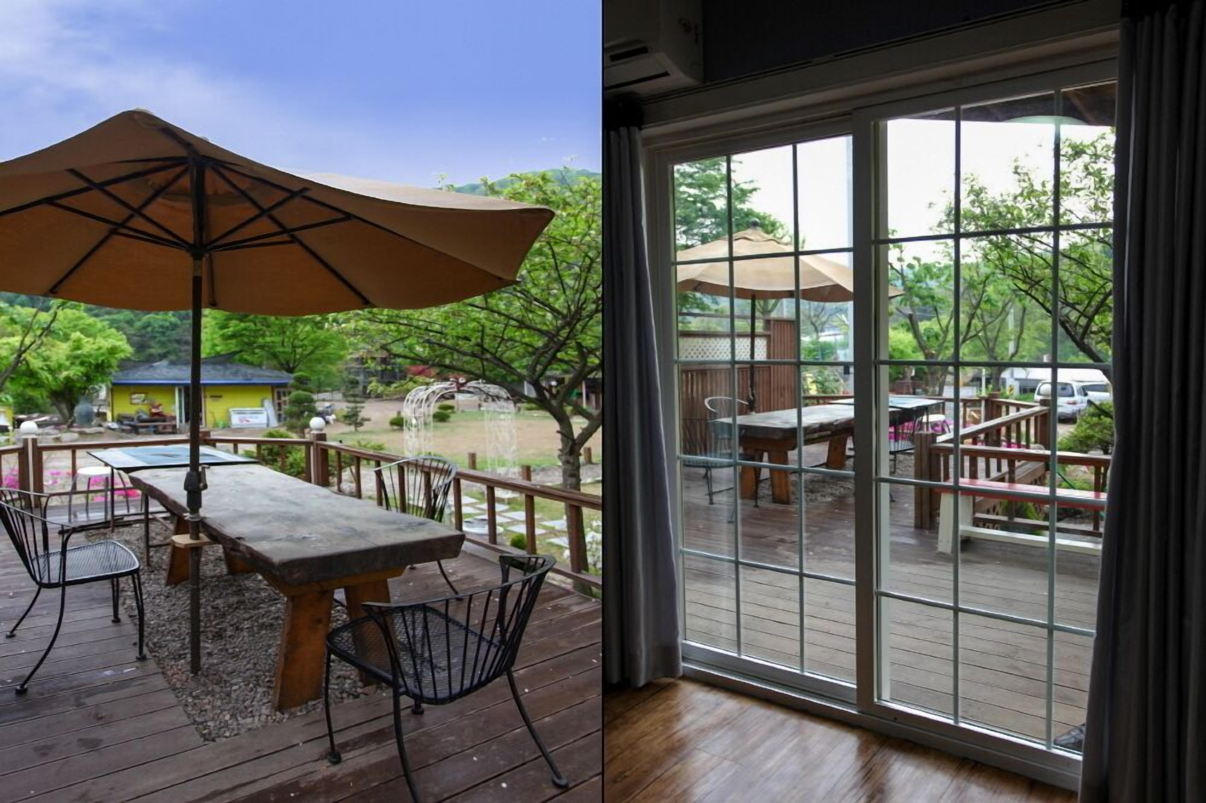 Une terrasse en bois, dotée de mobilier d’extérieur et d’un grand parasol, et une vue, à travers une porte vitrée, sur une autre terrasse aménagée de la même manière.