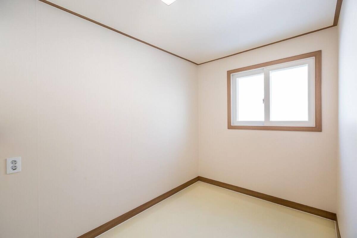 A room with a single window, a visible electrical outlet, and a corner with a wooden trim.