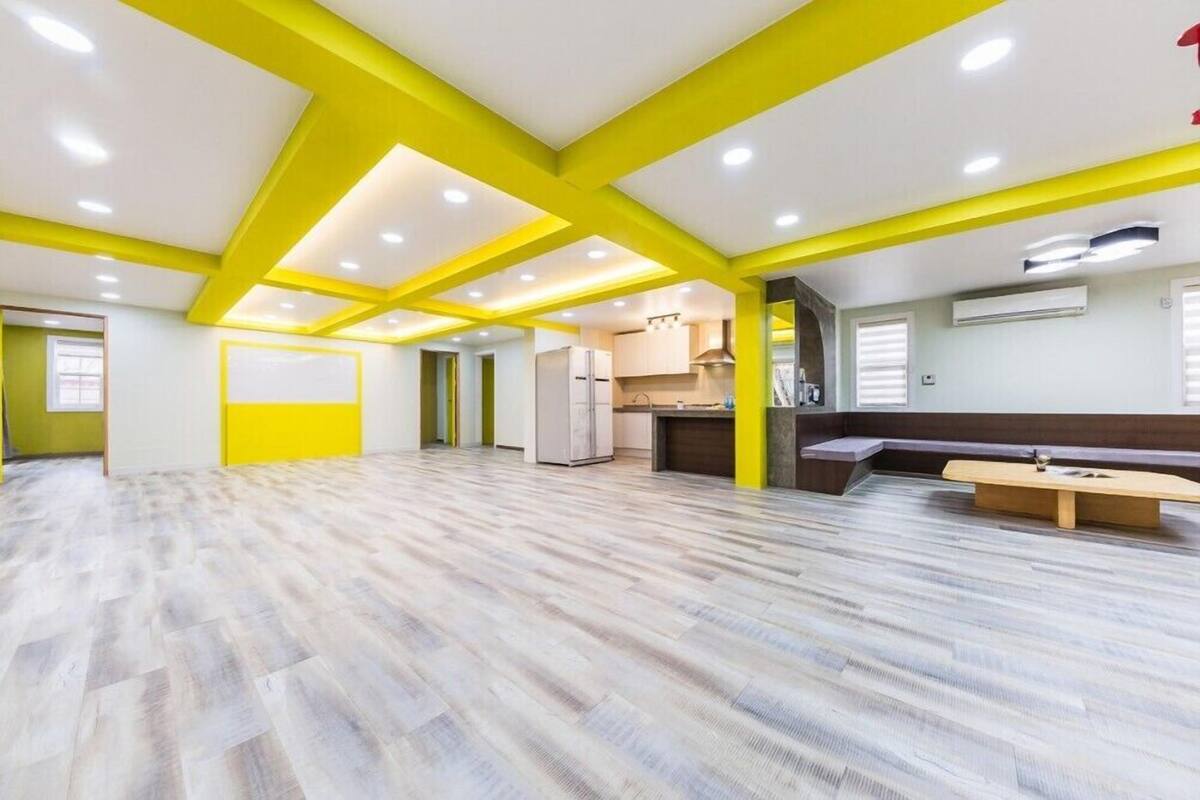 A spacious room with a wooden floor, a kitchen area, and a seating area with a bench.