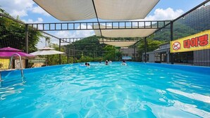 Una piscina interior con gente nadando, rodeada por una zona sombreada y un edificio con un letrero.
