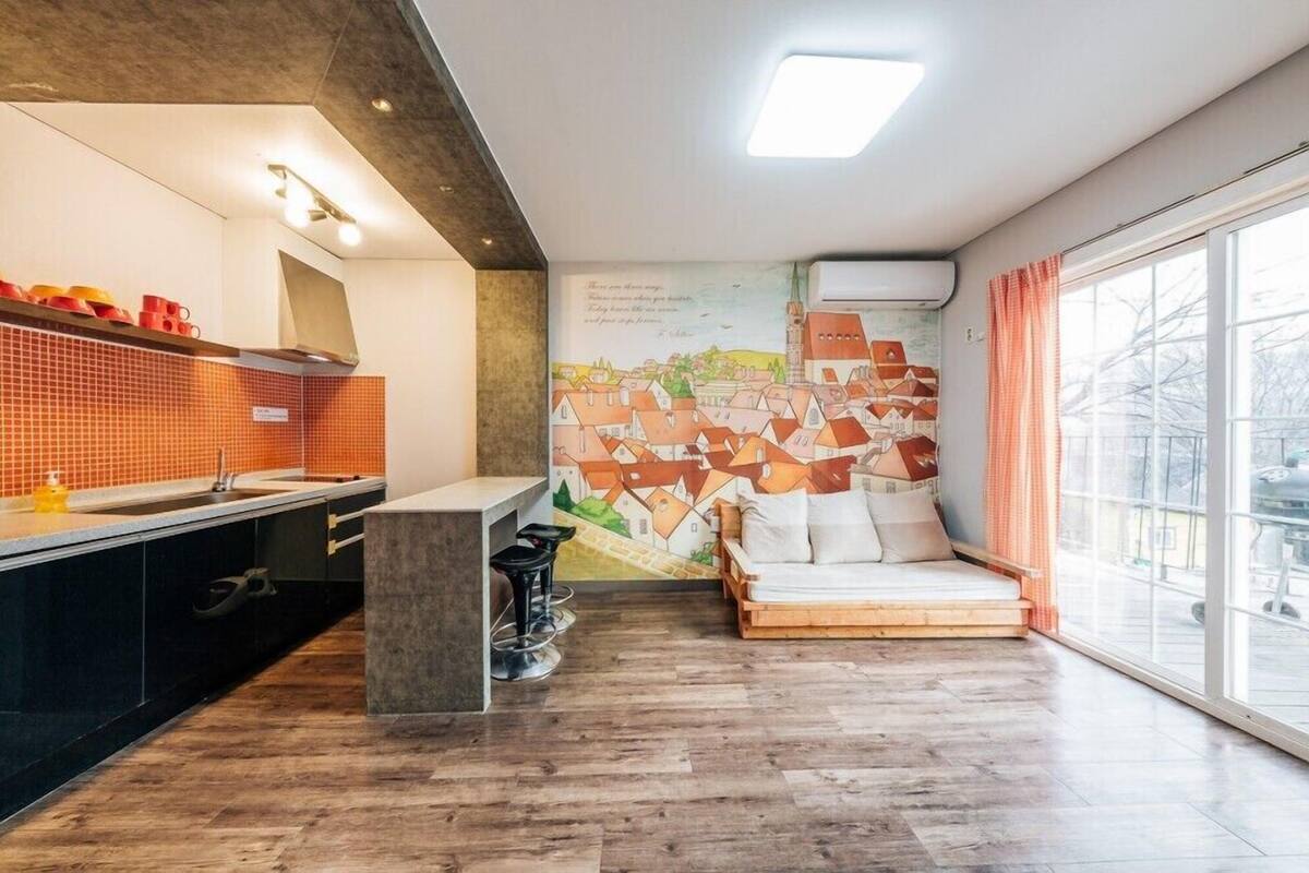 A modern kitchen with a large window, a mural of a town, and a cozy seating area.