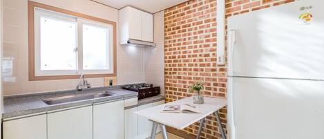 Una cocina con gabinetes blancos, un lavamanos doble, una estufa a gas y un refrigerador.