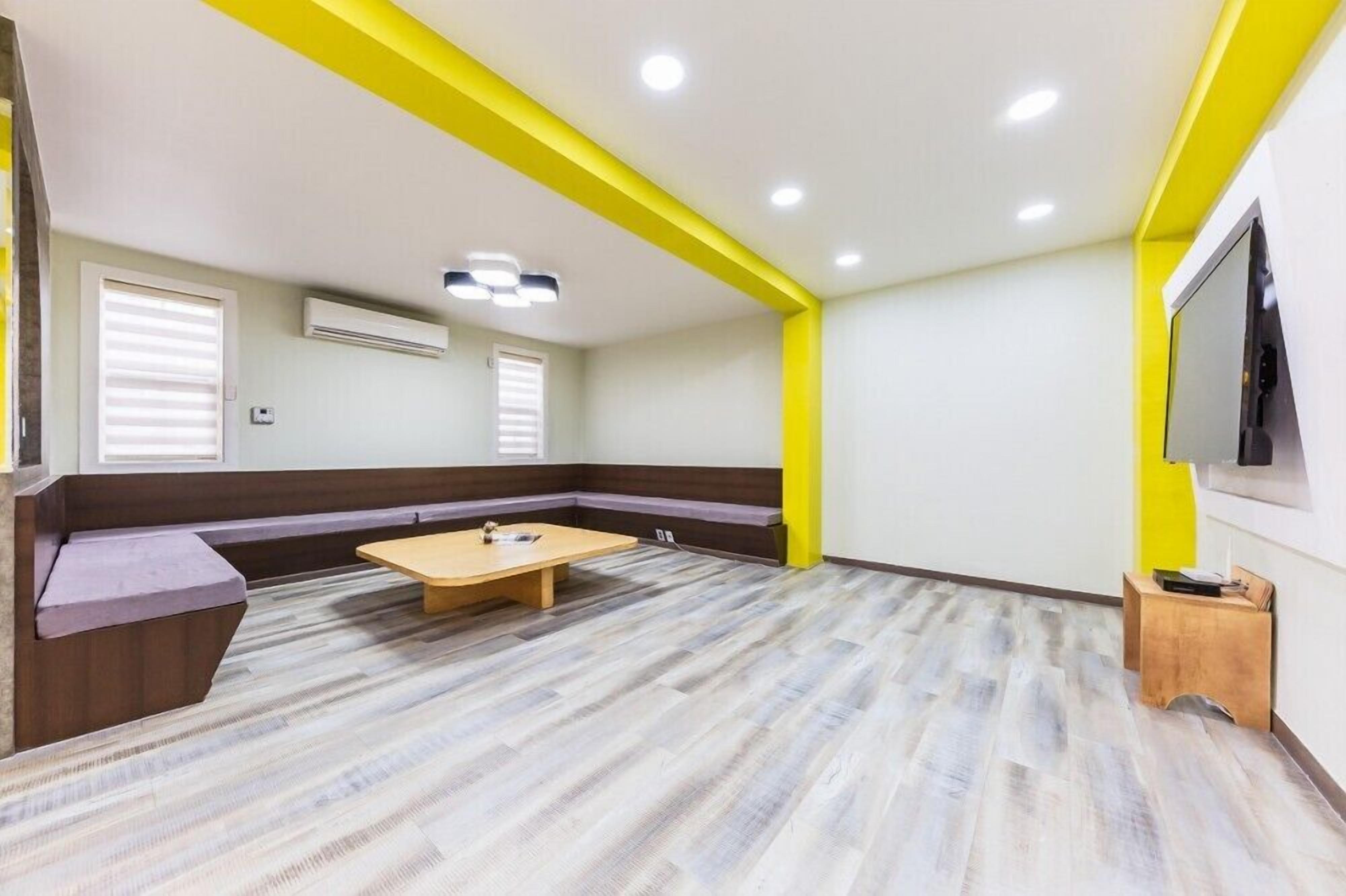 A room with a wooden floor, a bench, a table, and a TV mounted on the wall.