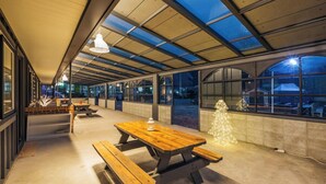 Un espacio interior amplio con techo alto, ventanas grandes y una mesa de picnic de madera.