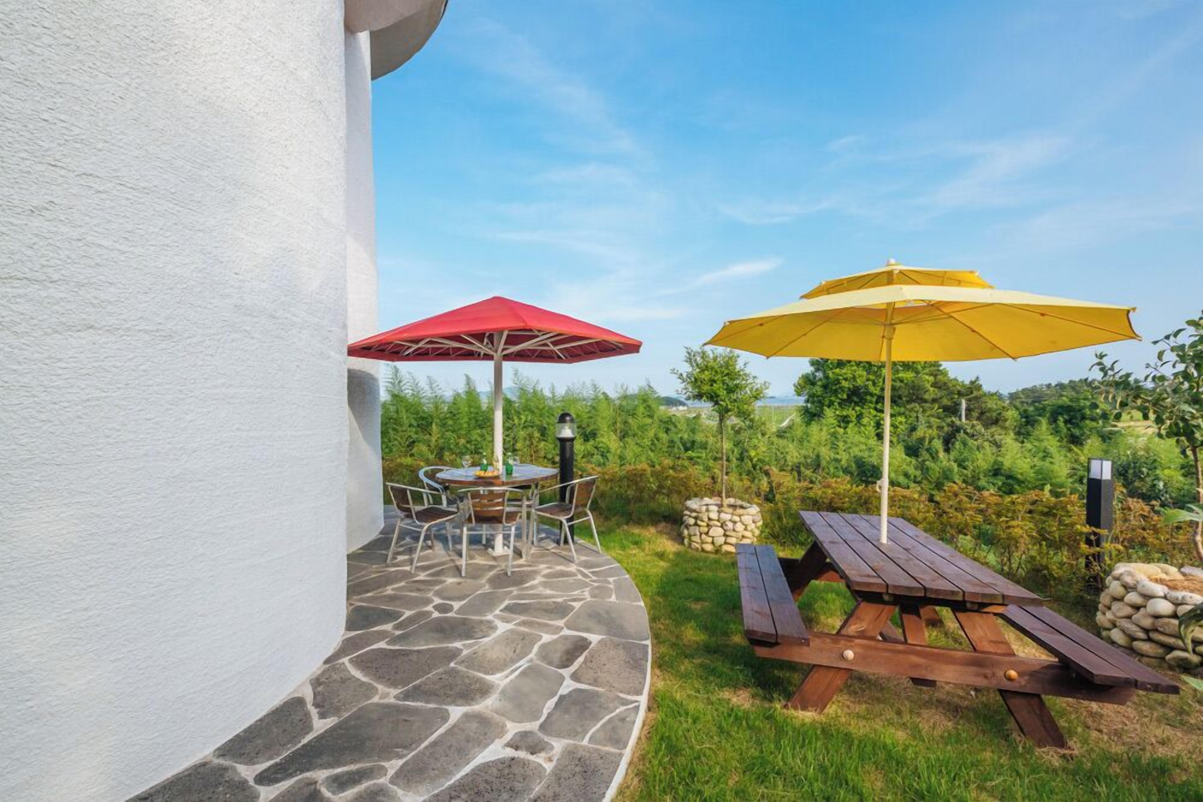 A patio area with a stone floor, a round table with chairs, and two umbrellas.