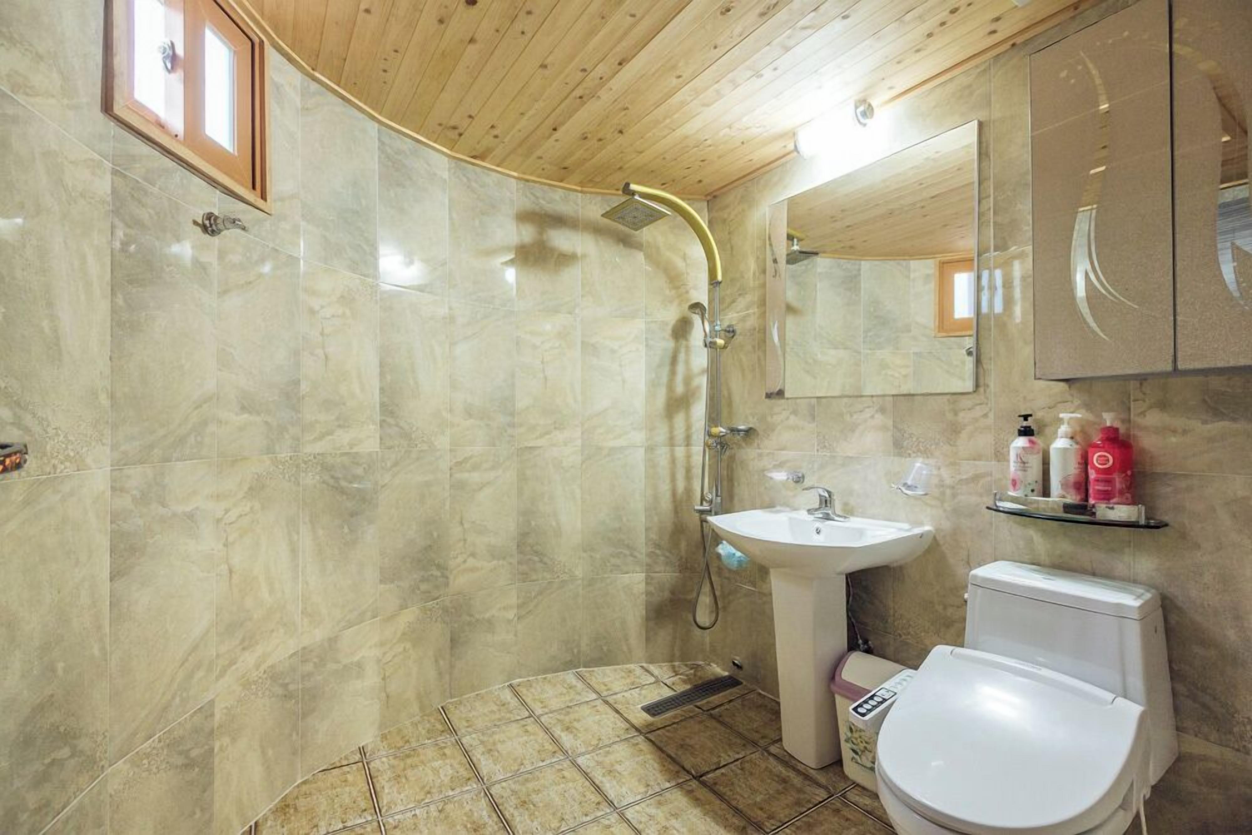 A bathroom with a shower, sink, toilet, and marble walls.