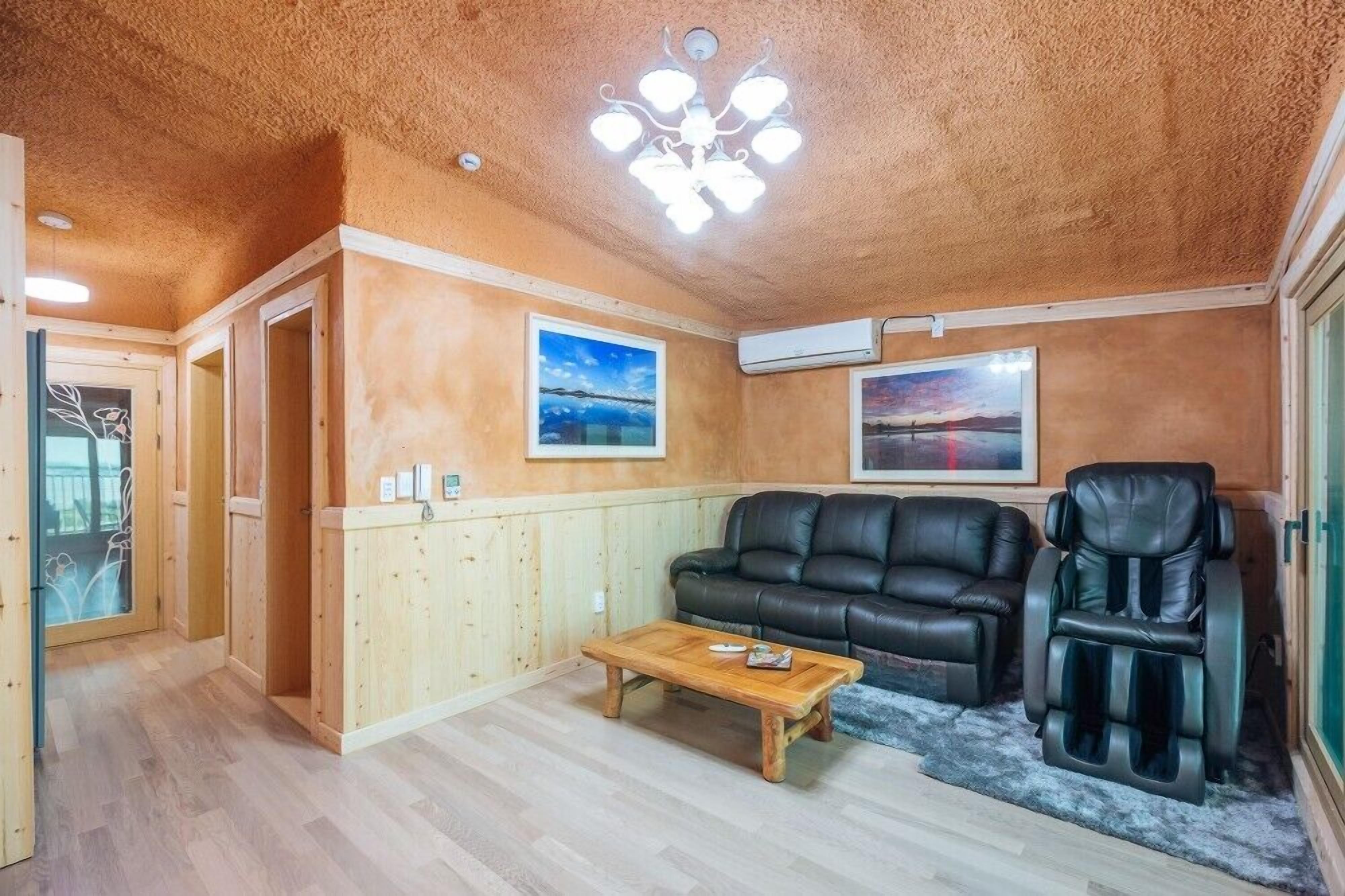 Un salon chaleureux avec un plancher en bois, un canapé en cuir noir, un fauteuil massant et deux tableaux encadrés accrochés aux murs.
