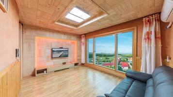 Un salon spacieux avec une grande fenêtre, un plafond en bois et un canapé noir.