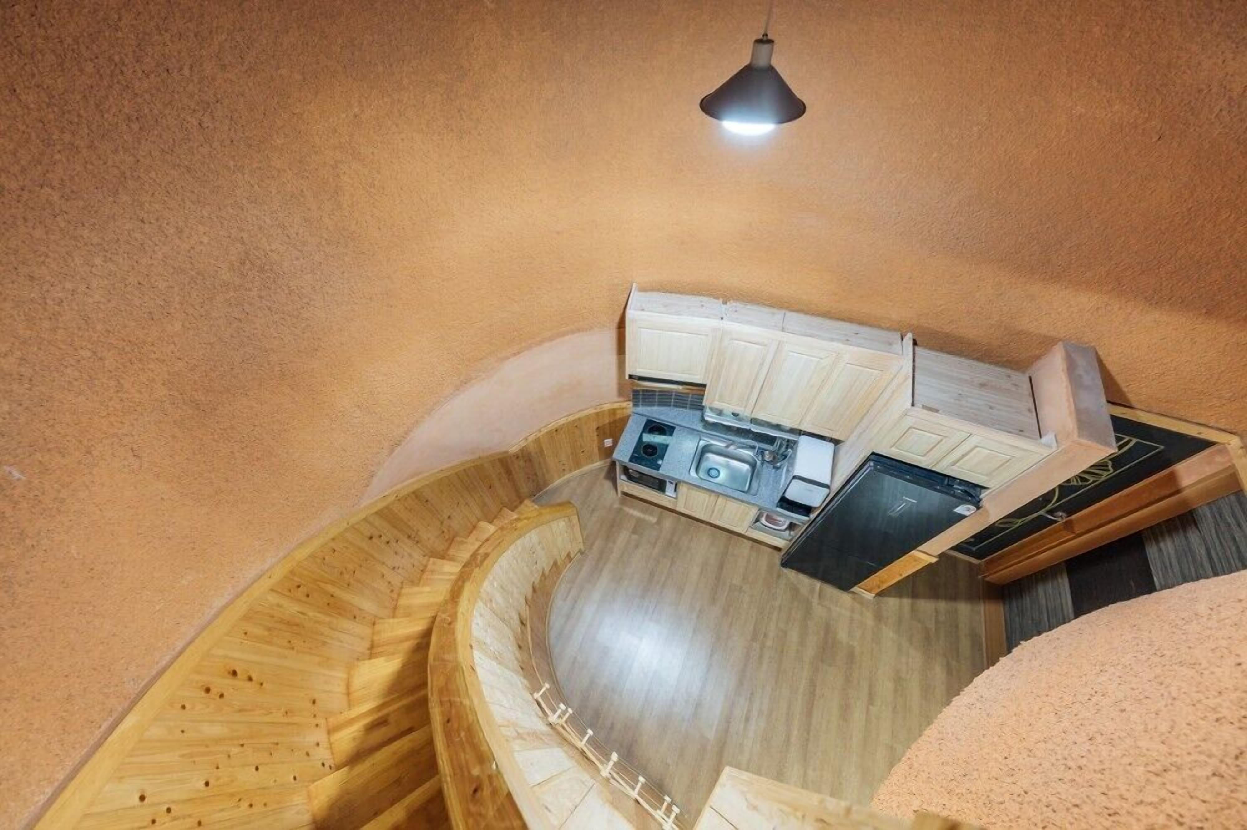 Una cocina compacta con fregadero, estufa y alacenas, ubicada en una habitación con paredes y piso de madera curvada.