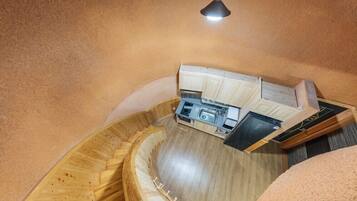 Una cocina compacta con fregadero, estufa y alacenas, ubicada en una habitación con paredes y piso de madera curvada.