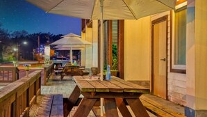 An outdoor patio area with wooden tables and benches, a large umbrella, and a view of the night sky. - Jebudo Olle Pension (Hwaseong)