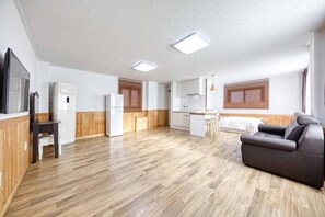Une pièce moderne et bien éclairée, dotée d’un plancher en bois, d’un canapé, d’une petite table et d’un coin cuisine avec des armoires en bois et un réfrigérateur.
