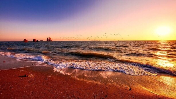 A beach with waves, a sunset, and rock formations in the distance. - Jebudo Olle Pension (Hwaseong)