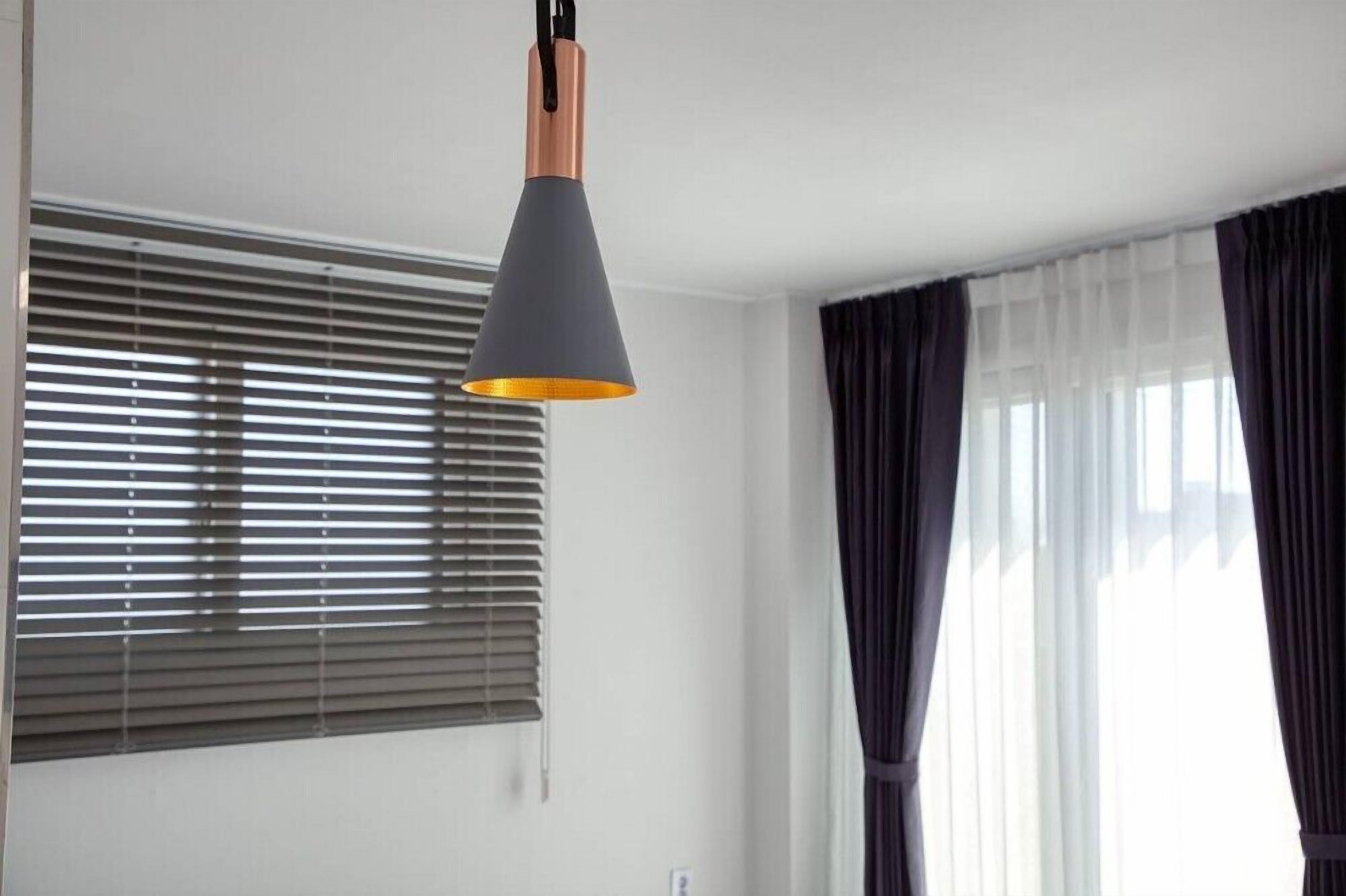 Ein Zimmer mit einer Deckenleuchte, einem Fenster mit Jalousien und einem Vorhang.