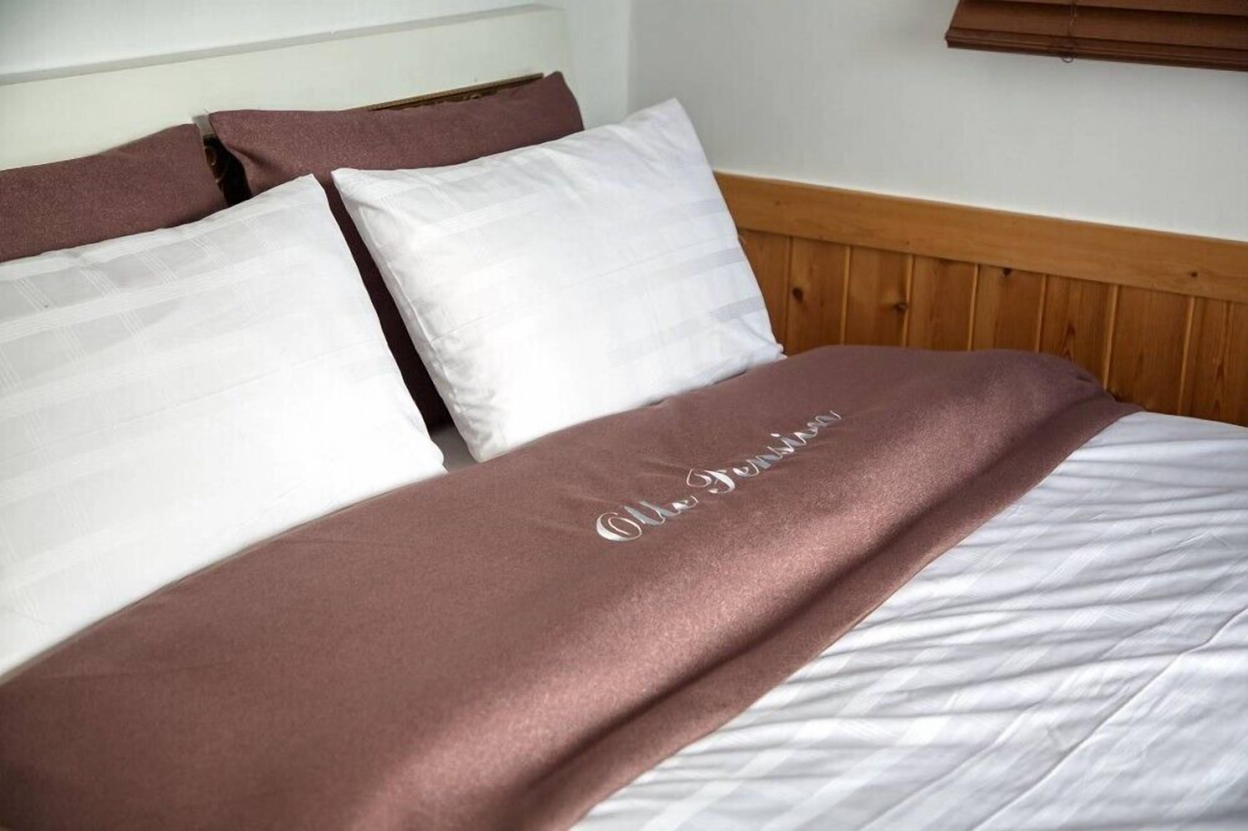 Uma cama com colcha branca e marrom, cabeceira de madeira e travesseiro branco.