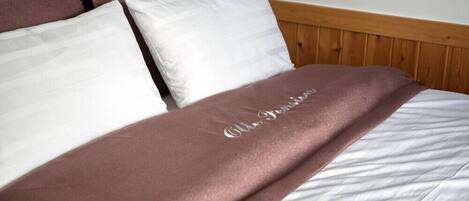 Uma cama com colcha branca e marrom, cabeceira de madeira e travesseiro branco.