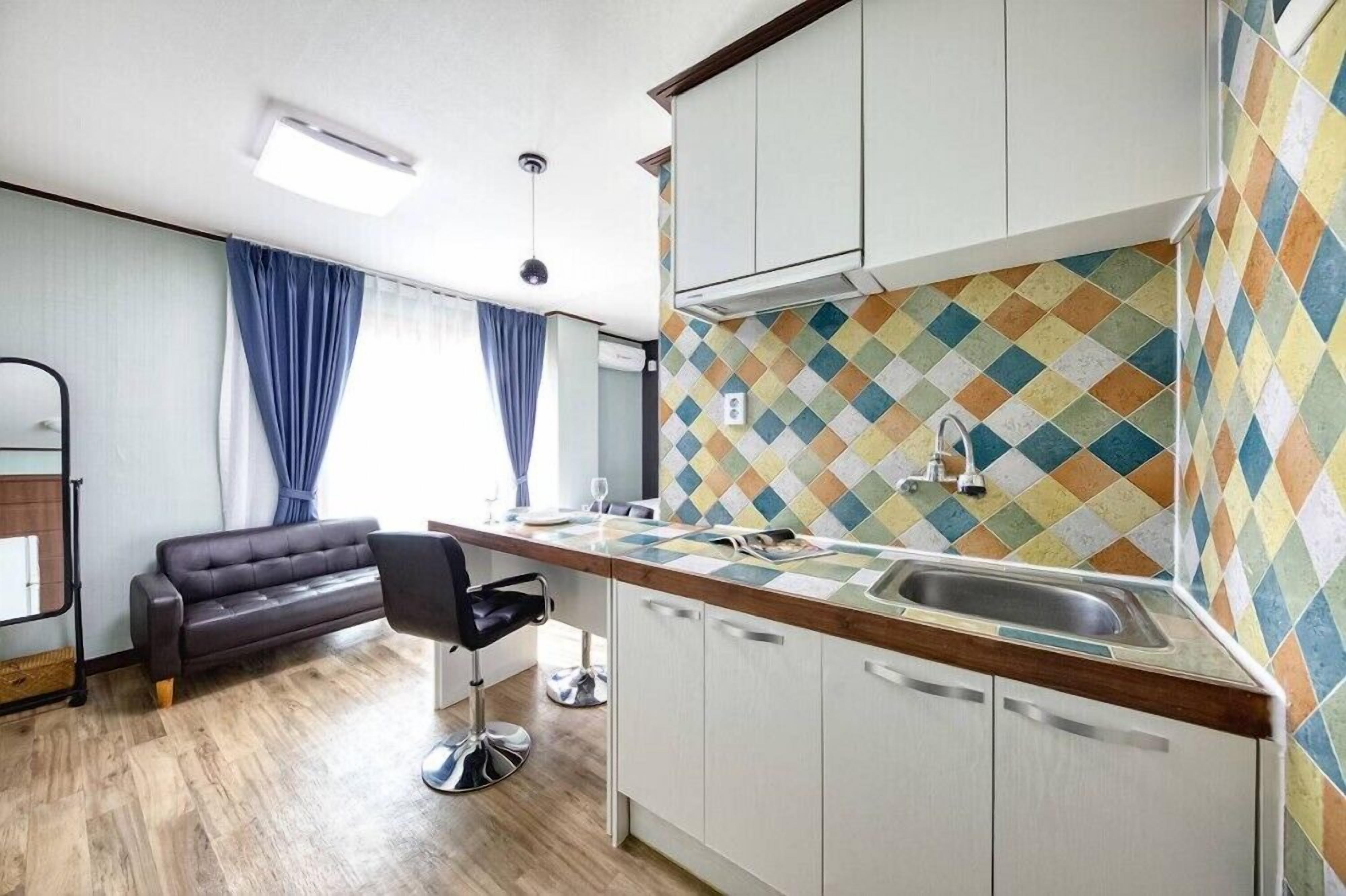 Una cocina compacta con diseño moderno, que destaca un salpicadero con llamativos diamantes, encimera de madera y armarios blancos.