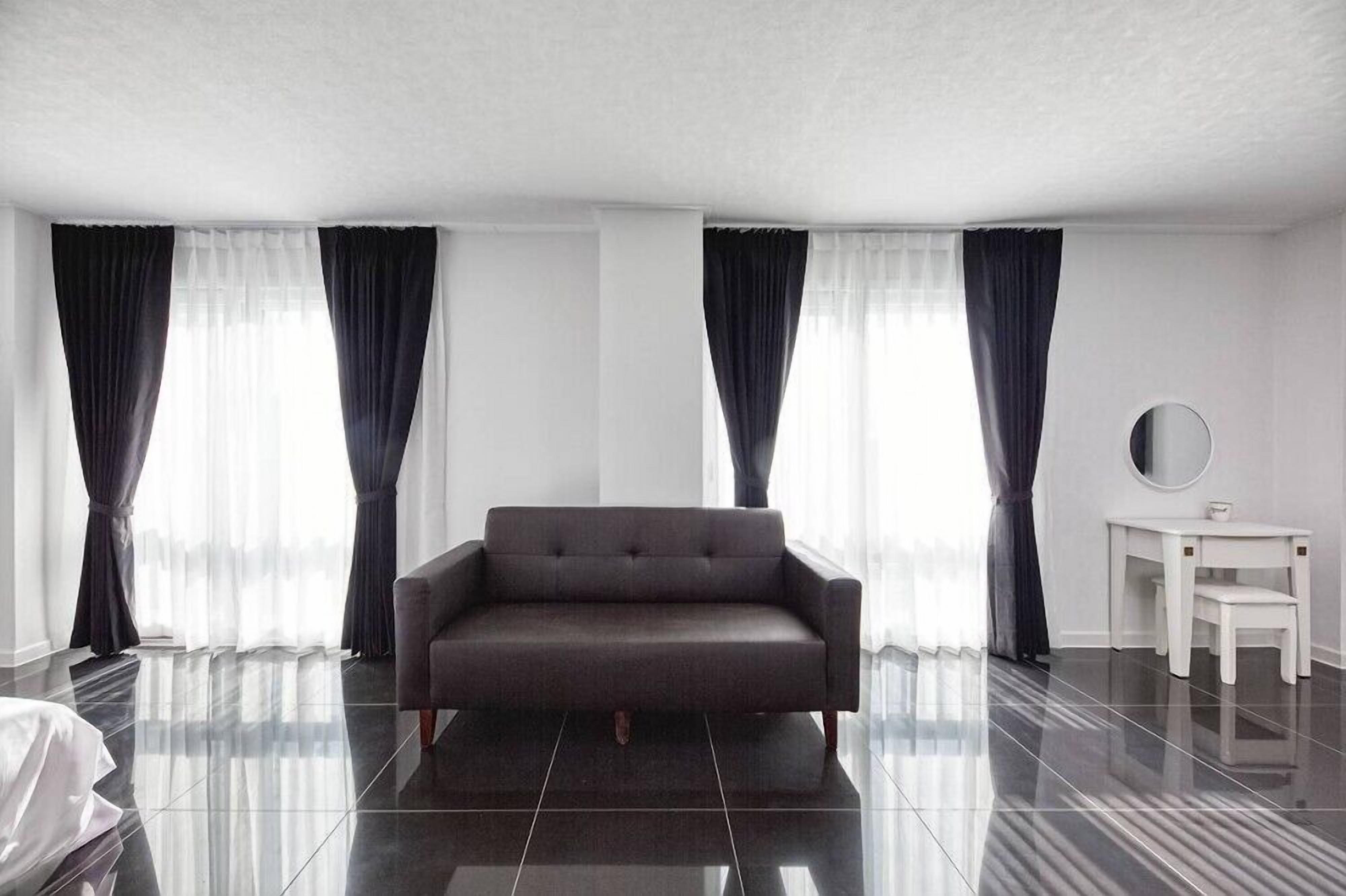 Une chambre d’hôtel moderne avec un canapé gris foncé, un miroir rond blanc et une petite table blanche.