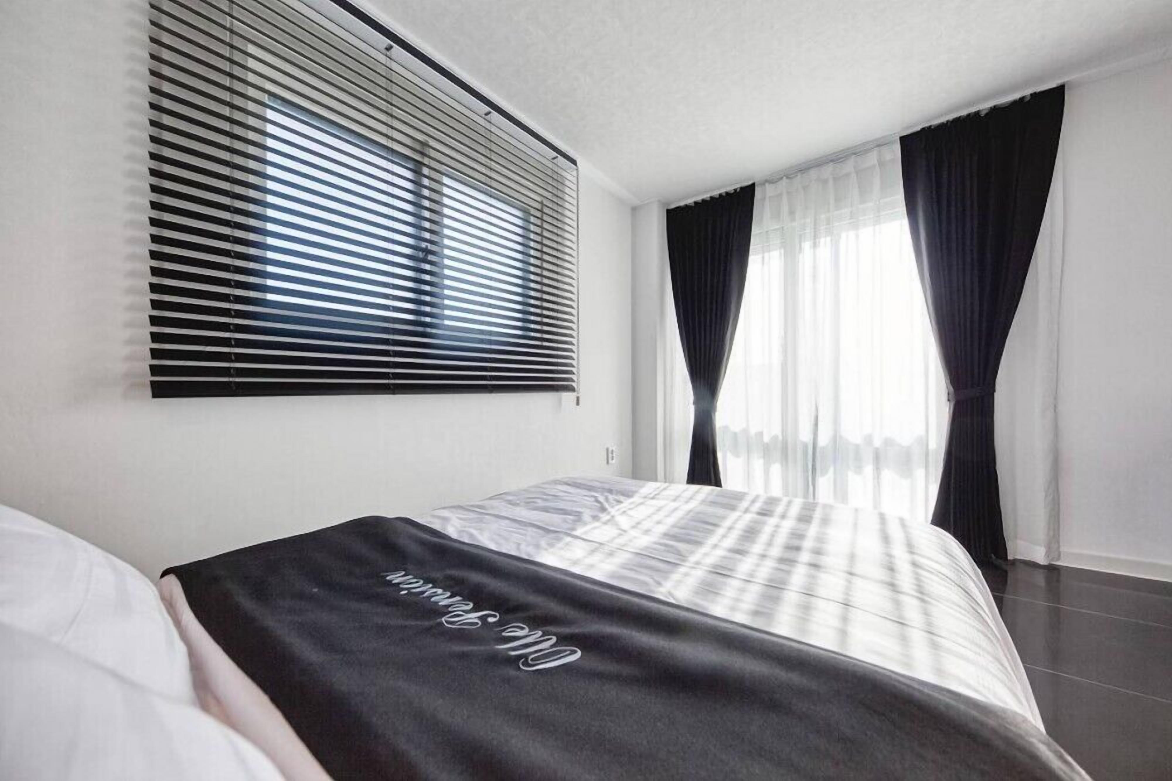 Une chambre d’hôtel avec un lit, une fenêtre avec des stores et un rideau.