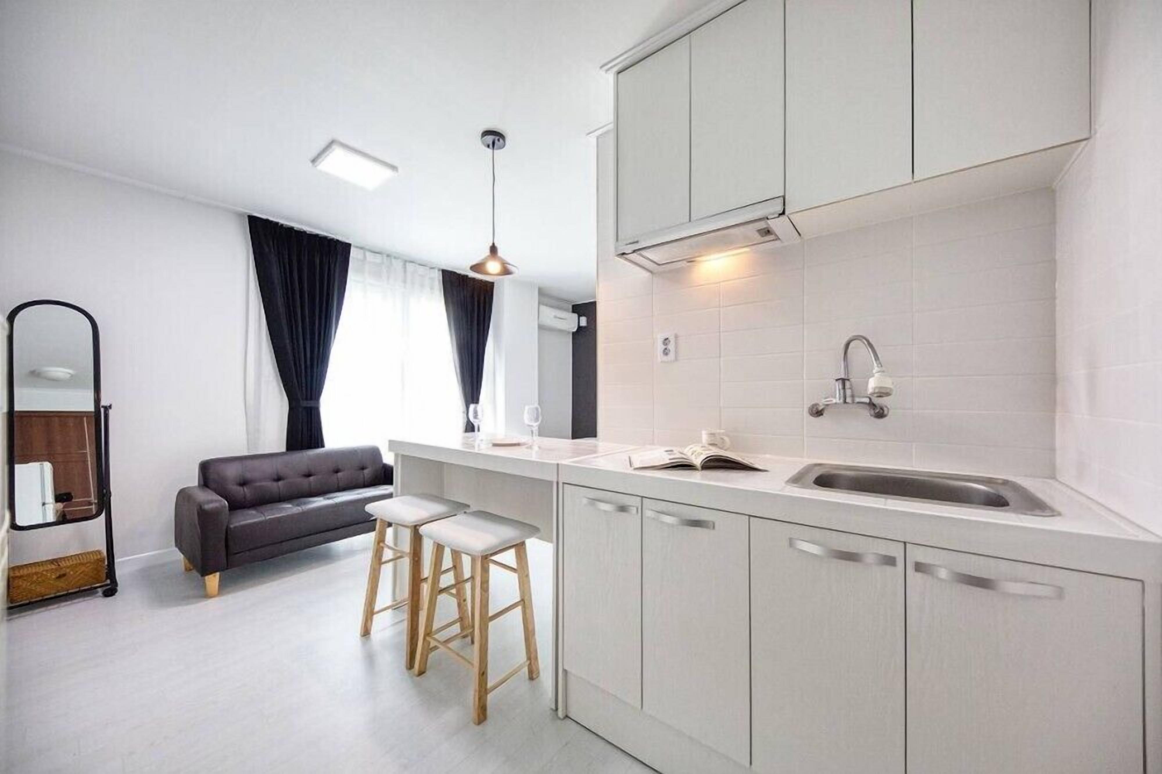 Eine moderne Küche mit weißen Schränken, einer integrierten Spüle und einem Essbereich mit einer Couch und Hockern.