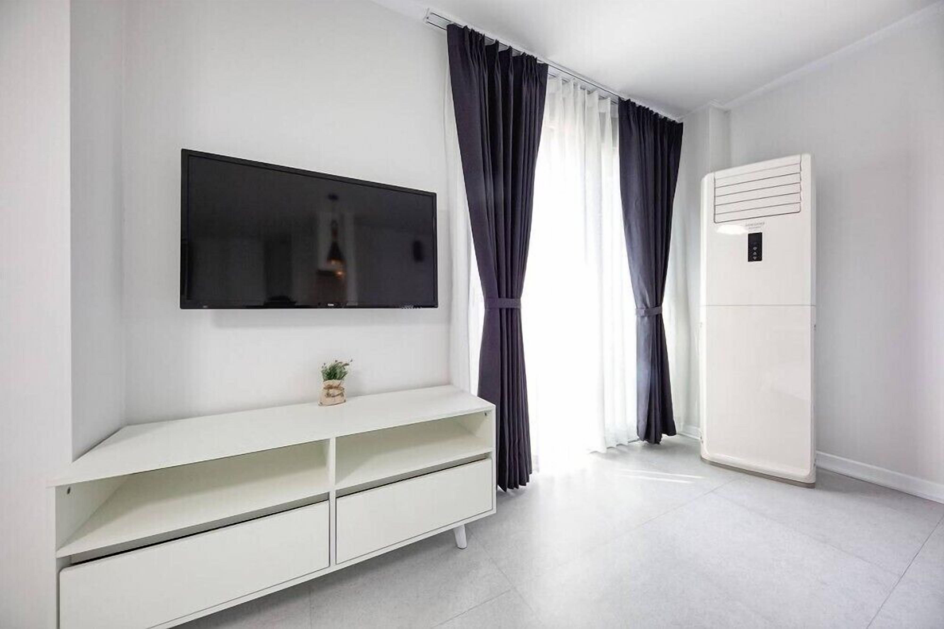 Una sala moderna con un televisor de pantalla plana montado en la pared, un mueble de entretenimiento blanco y un equipo de aire acondicionado blanco.