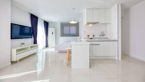 A modern, minimalist living space with a flat-screen TV, a small dining area, and a kitchenette. - Jebudo Olle Pension (Hwaseong)