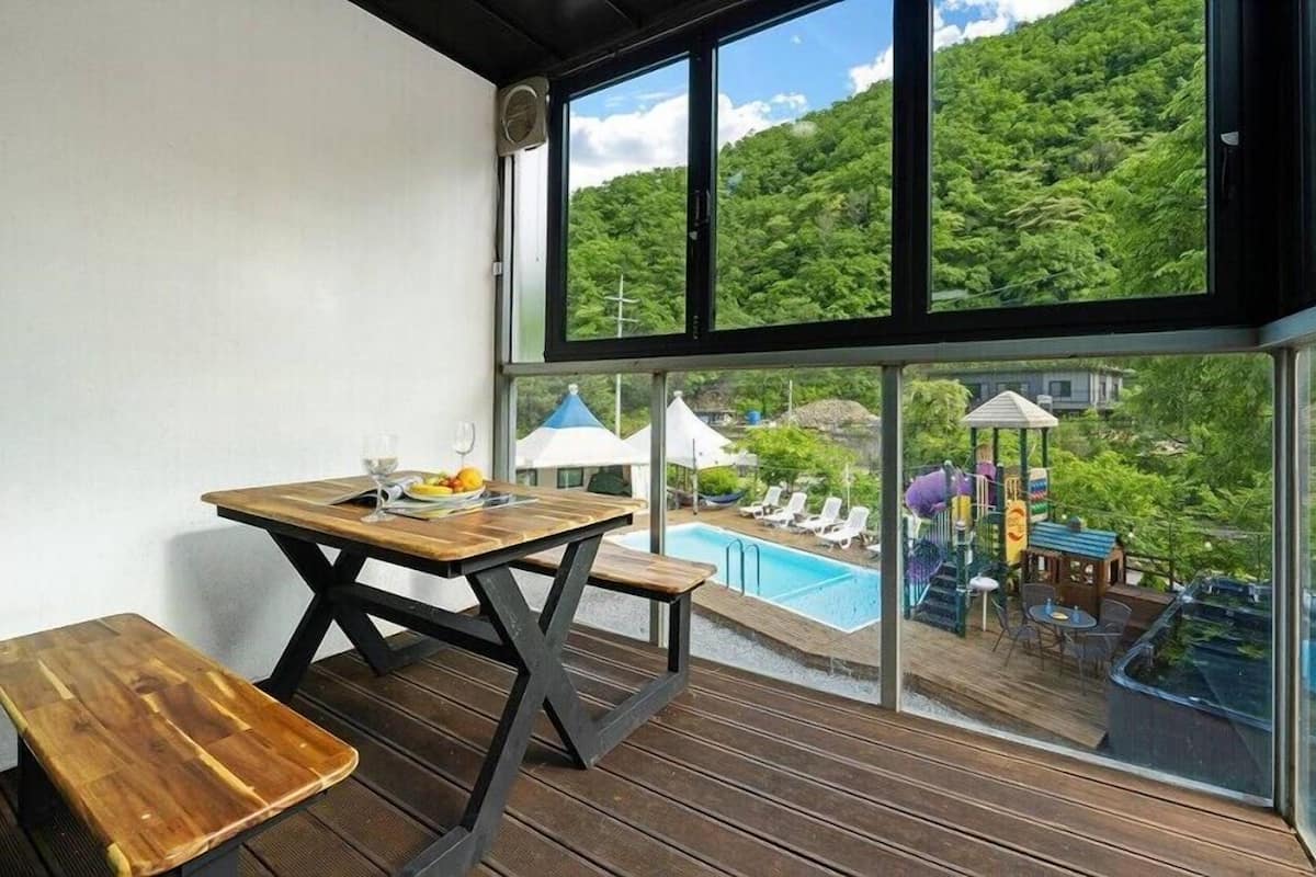 Un balcón con mesa y banco de madera, piscina y parque infantil.