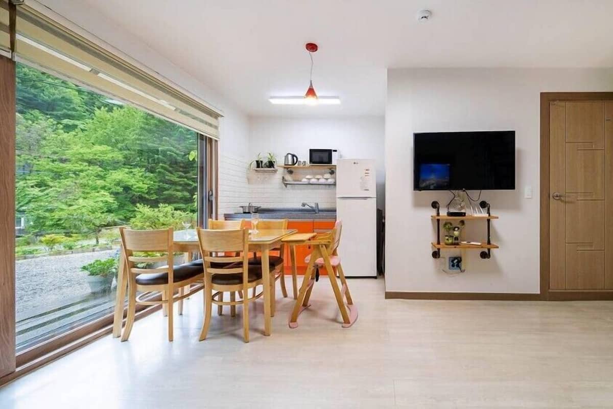 Una cocina moderna con comedor, televisor montado en la pared y un amplio ventanal con vistas a zonas verdes.