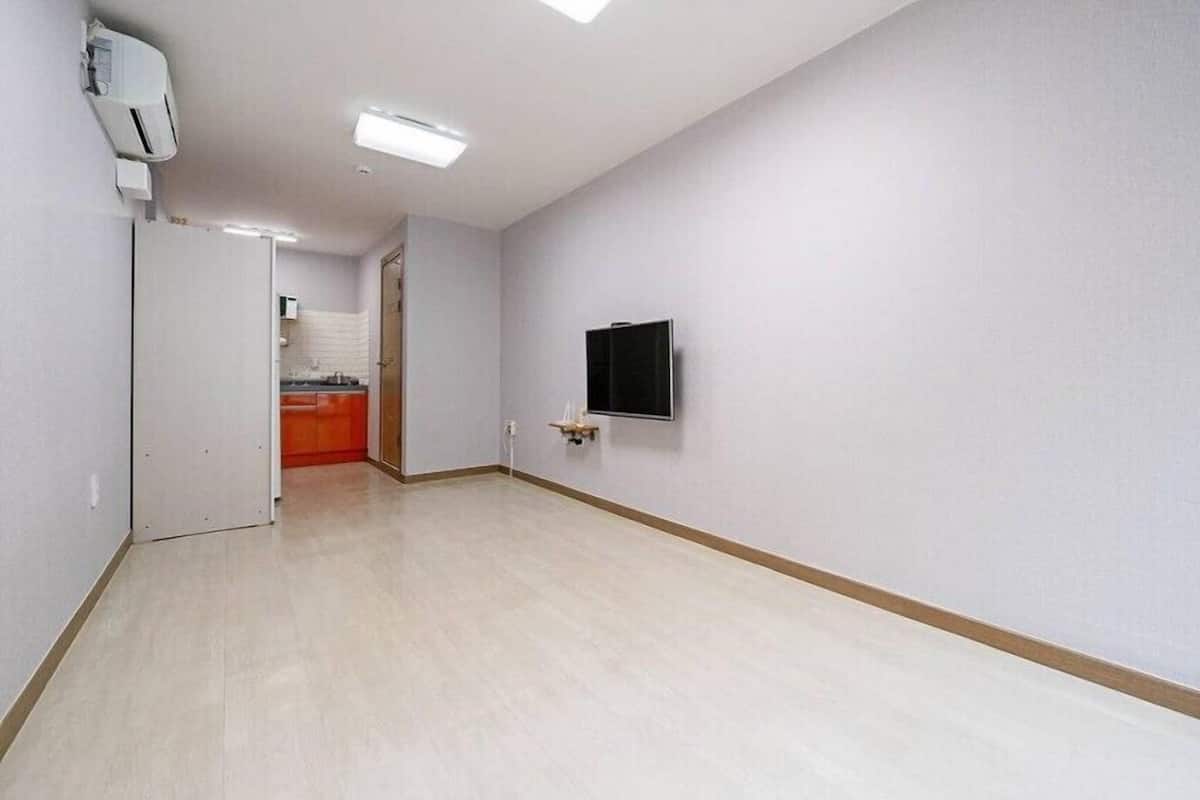 Una habitación amplia y vacía con piso de tonos claros, un televisor de pantalla plana montado en la pared y una unidad de aire acondicionado instalada en el techo.