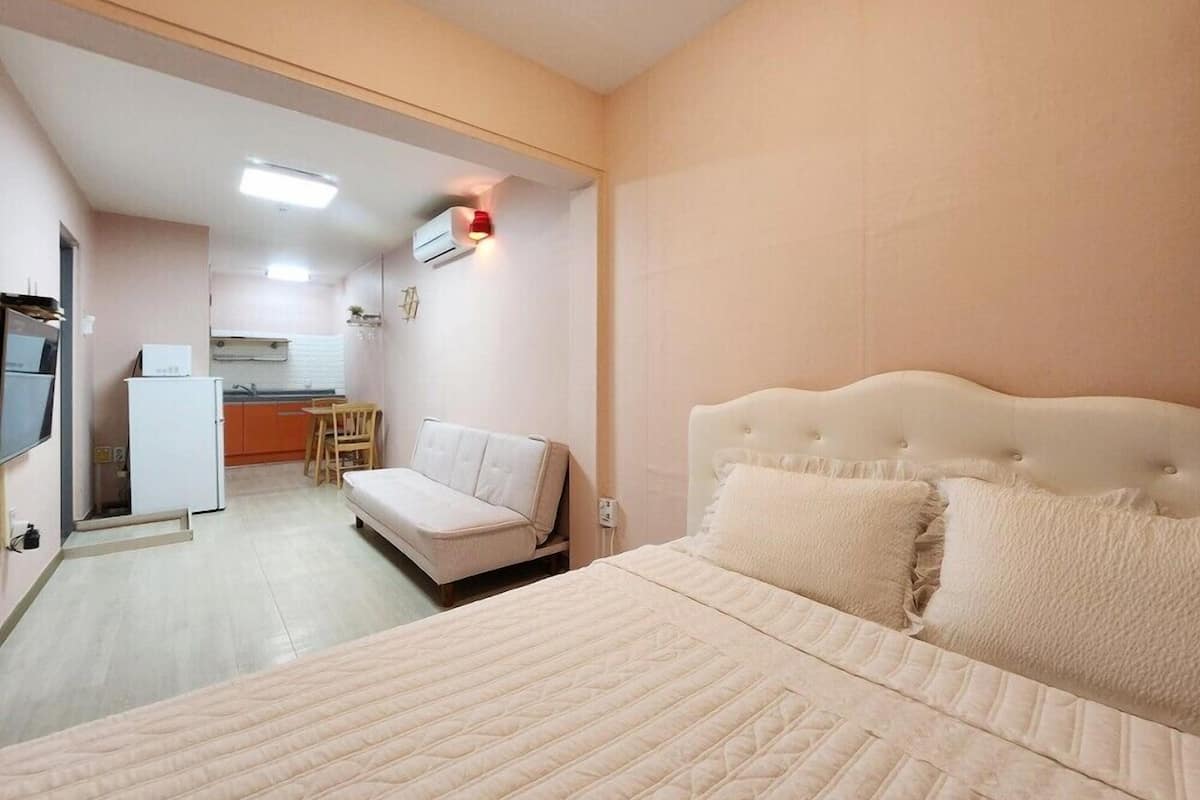 Un dormitorio con una cama, un sofá y una kitchenette al fondo.