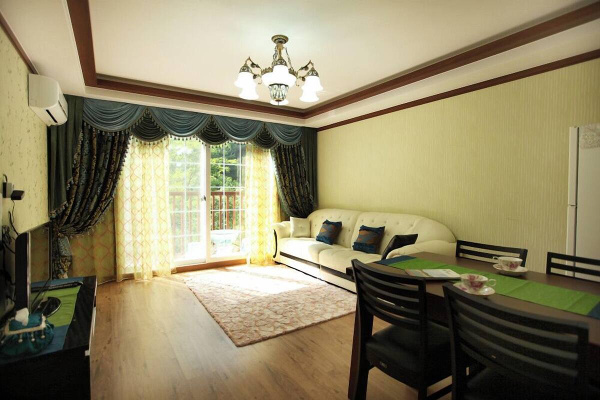 A living room with a sofa, dining table, chairs, a chandelier, and curtains.