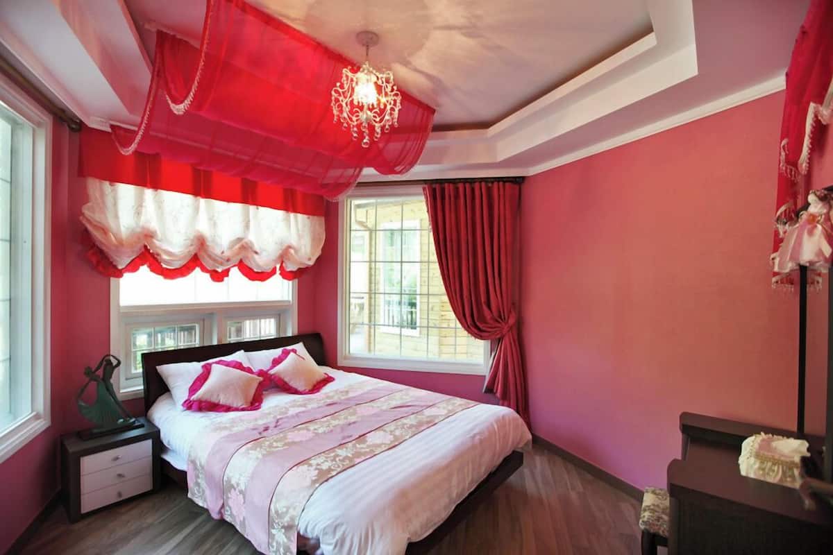 A bedroom with a bed, a nightstand, a dresser, a chandelier, and a window with curtains.