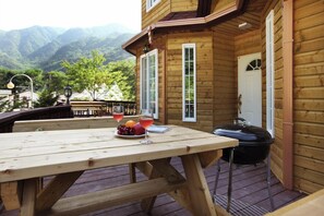 A wooden deck with a table set for two, a grill, and a scenic mountain view. - White Village Pension (Inje)
