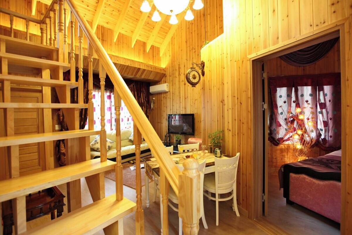 A wooden interior with a staircase, a dining area, a TV, and a bed with curtains.