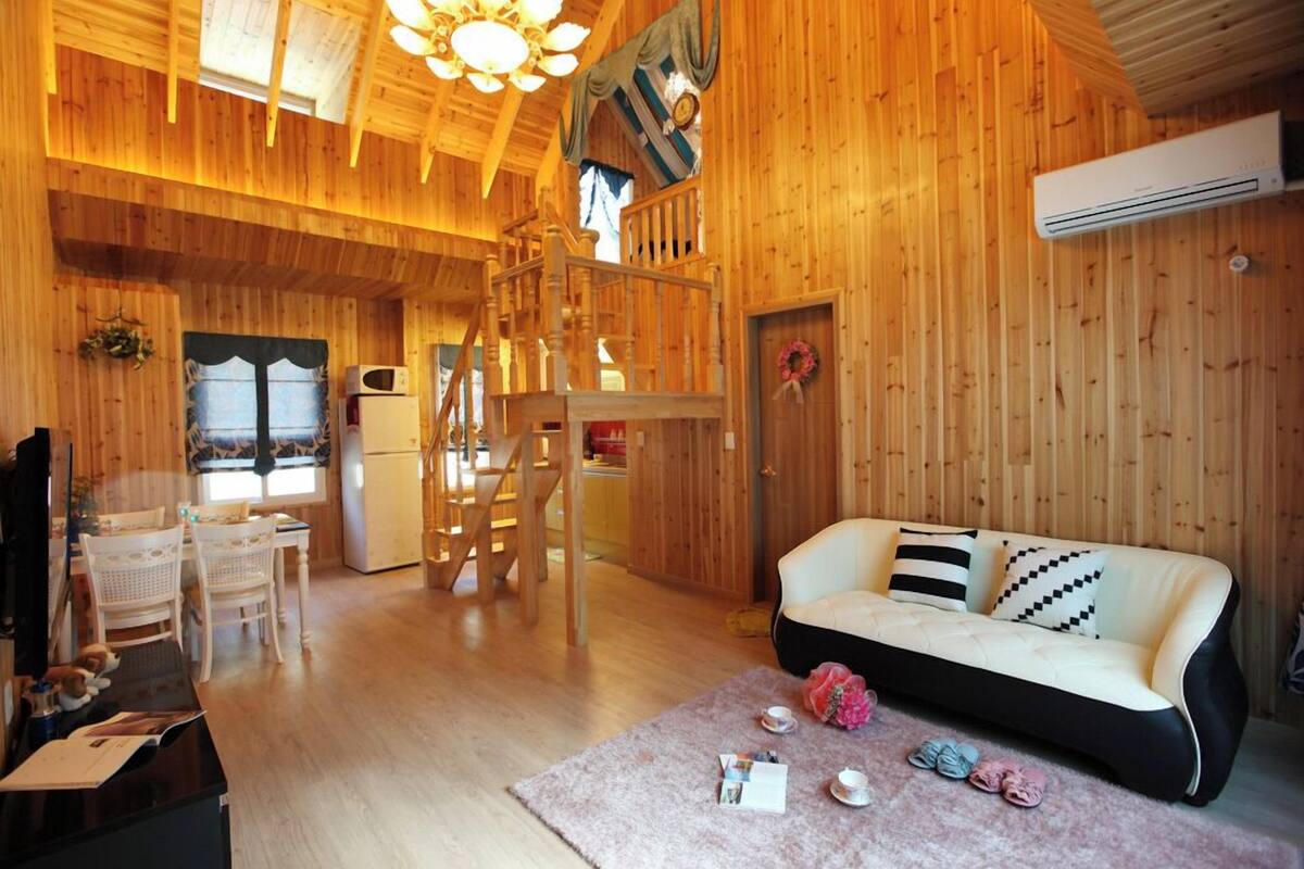 A cozy wooden cabin interior with a sofa, dining table, chairs, and a staircase.