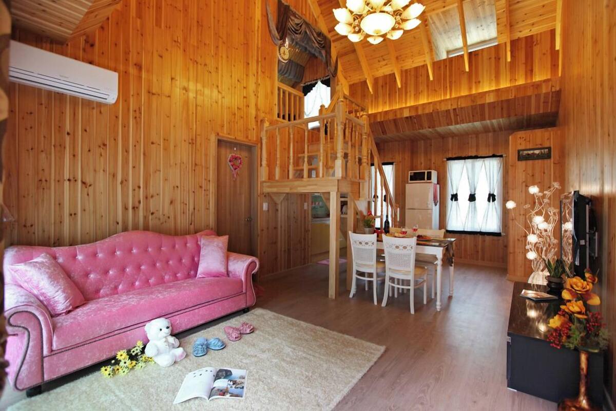 A wooden interior with a pink sofa, a dining area, and a staircase.