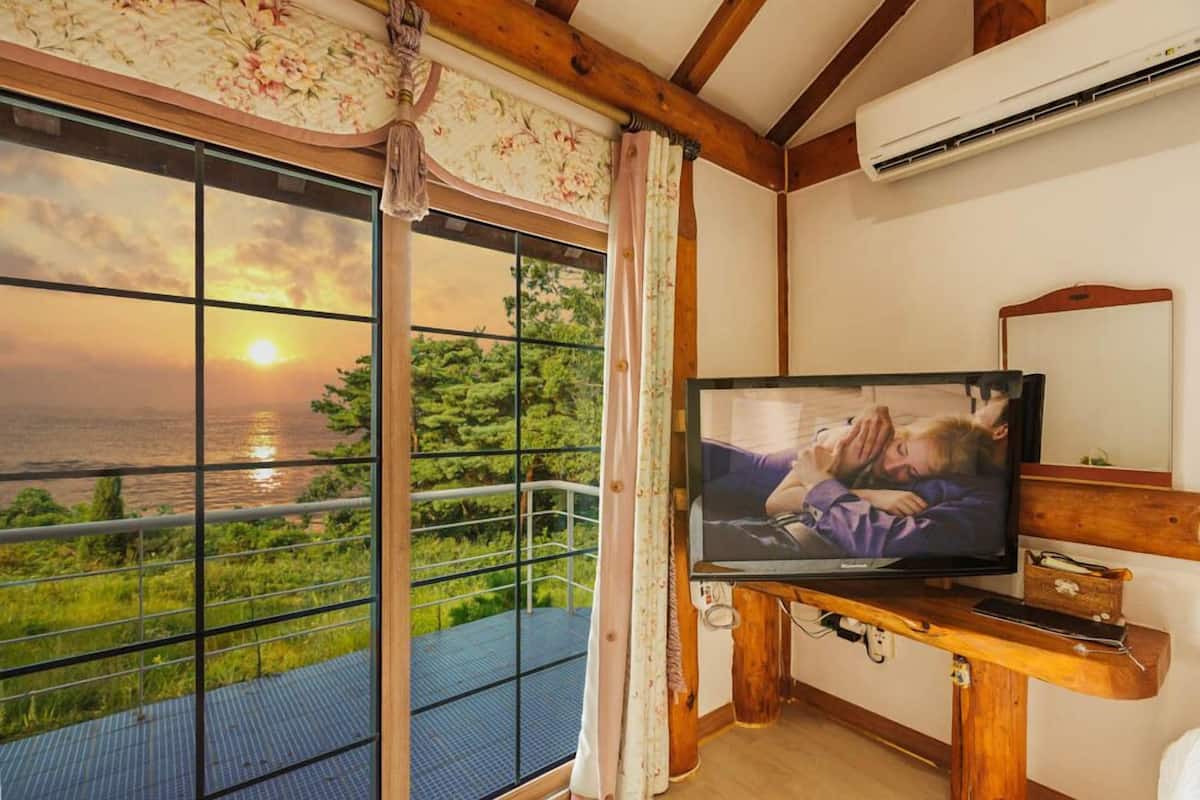 Huoneessa on suuri ikkuna, josta avautuu upea näkymä auringonlaskuun veden yllä. Huoneessa on myös televisio, joka on sijoitettu puiseen jalustaan, sekä ilmastointilaite seinällä.