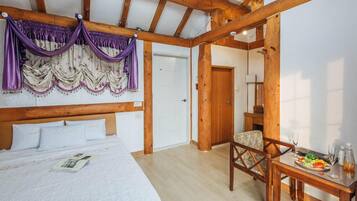 Un dormitorio con techo de madera, una cama con ropa de cama blanca, una silla, una mesa con una bandeja de frutas y una puerta.