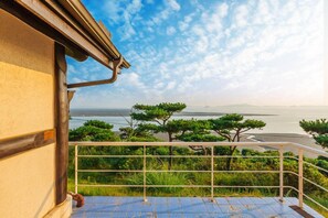 A balcony with a view of the sea and trees. - Sunset Pension (Incheon)