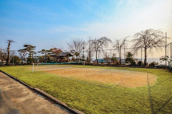 A sports court with a net, surrounded by a fence and trees.