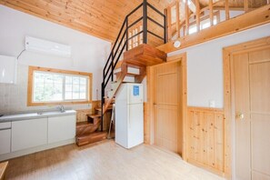 A kitchen with wooden flooring, a white refrigerator, a wooden staircase, and a window with a view of greenery. - Ulsan Paradise Pension (Ulsan)